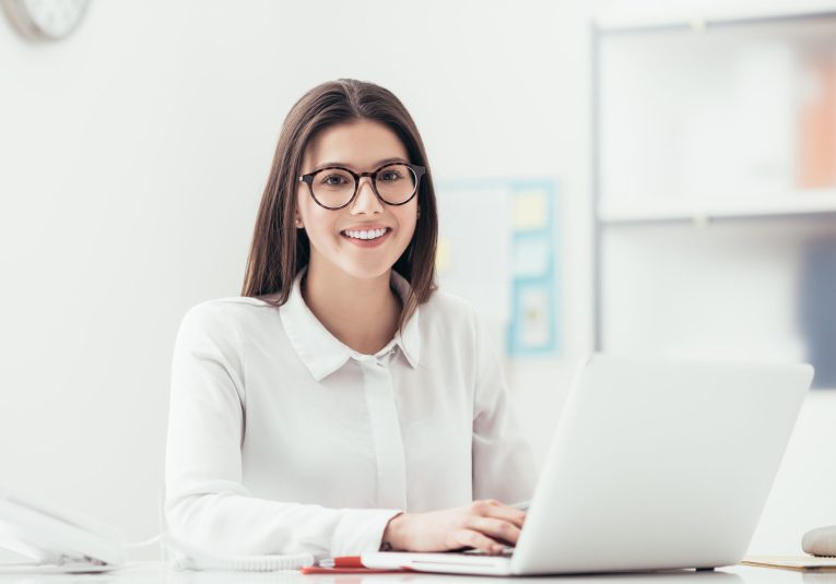 Young office worker Young woman working at office desk, she is typing on a laptop and smiling, job and career concept